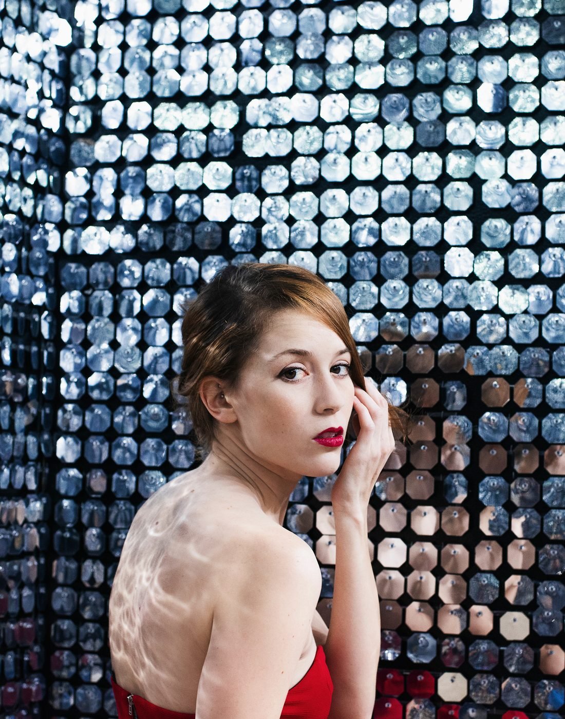 Model in a red sequin dress turning toward a mirrored wall