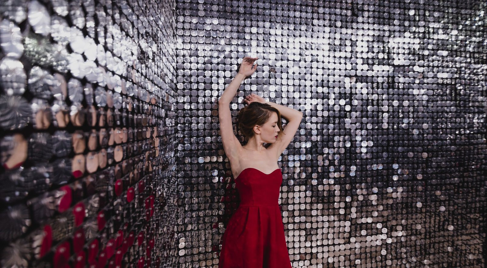 Model with arms raised in a red dress inside a mirrored sequin room
