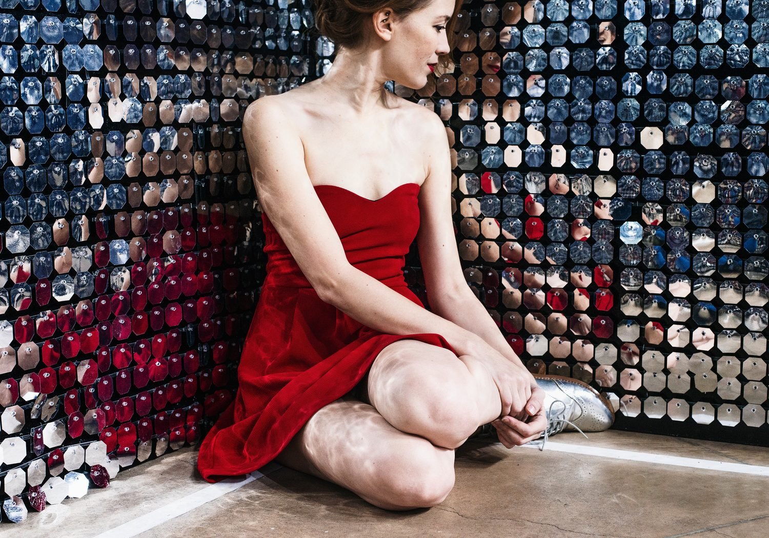 Model seated in a crimson column dress against a wall of mirrors
